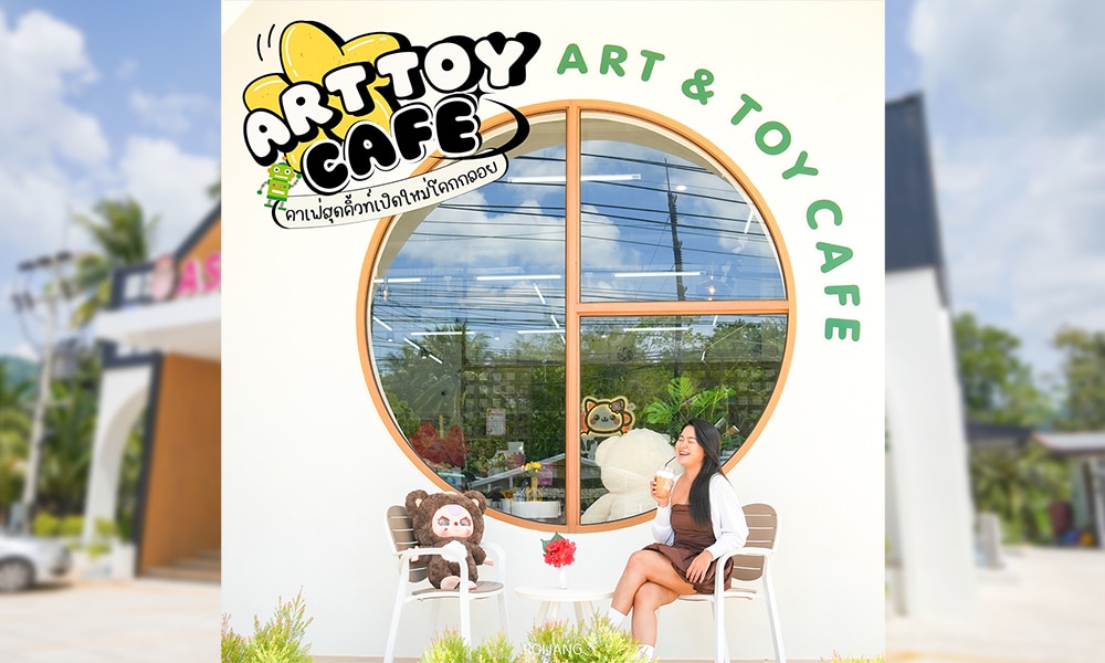 ผู้หญิงคนหนึ่งกำลังจิบเครื่องดื่มอยู่หน้า Art & Toy Cafe ซึ่งอยู่ข้างๆ ตุ๊กตาหุ่นของเล่นที่ตั้งตังค์ โลโก้ของร้านตั้งตระหง่านอยู่เบื้องหลัง.