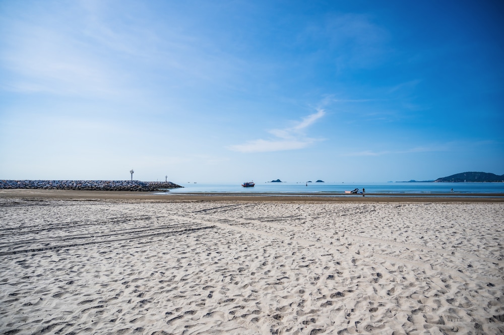 หาดทรายที่มีรอยยางใต้ท้องฟ้าสีครามใส ทะเลสงบเป็นฉากหลัง และเขื่อนกันคลื่นทางซ้าย สวรรค์อันเงียบสงบที่รวบรวมแก่นแท้ของที่เที่ยวหัวหิน. ที่เที่ยวหัวหิน 