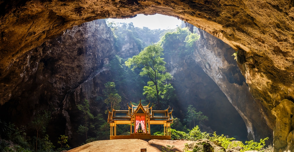 ศาลาเล็กๆ หรูหราตั้งอยู่ภายในถ้ำขนาดใหญ่ที่เปิดอยู่ในหัวหินที่เที่ยว  ที่เที่ยวหัวหิน ล้อมรอบด้วยกำแพงหินและความเขียวขจี แสงลอดเข้ามาจากด้านบน เน้นให้เห็นรายละเอียดของศาลา.