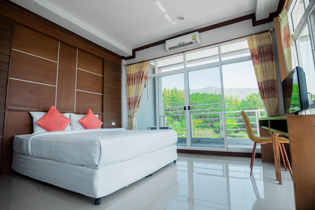 ห้องพักในโรงแรมทันสมัยพร้อมเตียงคู่ที่ตกแต่งอย่างประณีต โต๊ะ เก้าอี้  ที่พักเขาค้อ ทีวี หน้าต่างบานใหญ่ และระเบียงที่มองเห็นความเขียวขจีและภูเขา เหมาะสำหรับผู้ที่กำลังมองหาหาดเจ้าหลาวติดทะเลหรือประสบการณ์การพักผ่อนในหาดเจ้าหลาวที่ผ่อนคลาย.
