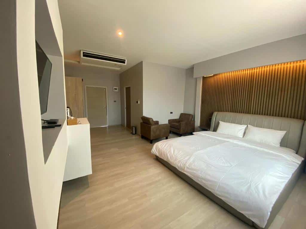ห้องพักในโรงแรมทันสมัยพร้อมเตียงขนาดใหญ่ เก้าอี้เท้าแขนสีน้ำตาล 2 ตัว ทีวีติดผนัง และผนังไม้ เหมาะ ที่เที่ยวแก่งคอย สำหรับการพักผ่อนหลังจากเที่ยวชมเมืองแก่งคอยหรือเยี่ยมชมที่เที่ยวชะอมแก่งคอย.