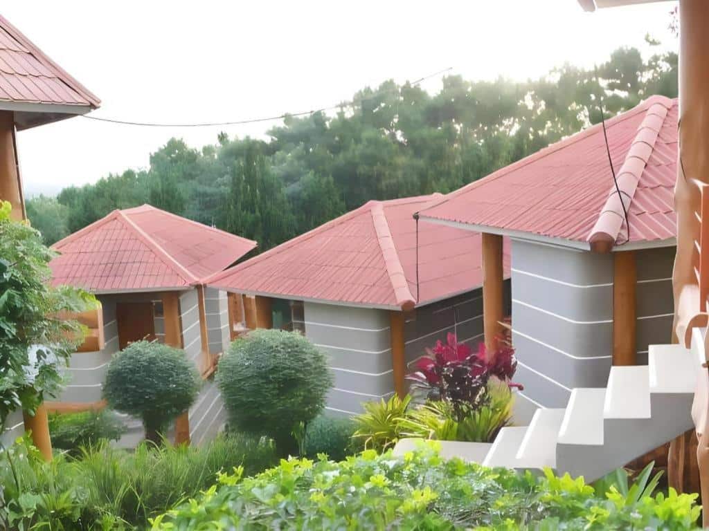 บ้านหลังเล็กๆ หลังคาสีแดง ผนังสี เขาค้อที่พัก เทาลายทาง ล้อมรอบด้วยพุ่มไม้และต้นไม้สีเขียว มีบันไดนำไปสู่ทางเข้าเพียงทางเดียว เหมาะสำหรับการพักผ่อนที่ ที่พักเจ้าหลาว ห่างจากชายหาดเพียงไม่กี่ก้าว.