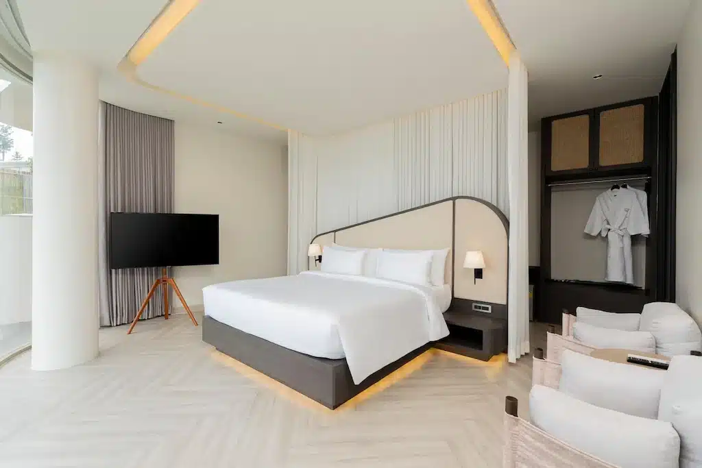 ห้องพักในโรงแรมทันสมัยพร้อมเตียงขนาดใหญ่ ทีวีจอแบน ตู้เสื้อผ้าแบบเปิดพร้อมเสื้อคลุม เก้าอี้เท้าแขน  ที่พักเขาค้อ และหน้าต่างสูงจากพื้นจรดเพดาน สถานที่พักผ่อนที่น่าดึงดูดใจสำหรับผู้ที่กำลังมองหาหาดเจ้าหลาวติดทะเลอย่างสะดวกสบายและมีสไตล์.