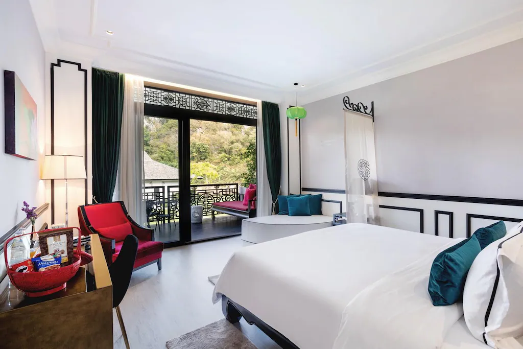 ห้องพักโรงแรมสไตล์โมเดิร์นใกล้ที่ ที่เที่ยวแก่งคอย เที่ยวชะอมแก่งคอย มีเตียงขนาดใหญ่ โต๊ะทำงาน เก้าอี้สีแดง และประตูระเบียงที่มองเห็นความเขียวขจี แสงธรรมชาติส่องเข้ามาในพื้นที่ และการตกแต่งแบบมินิมอลโดยเน้นสีขาวดำ.