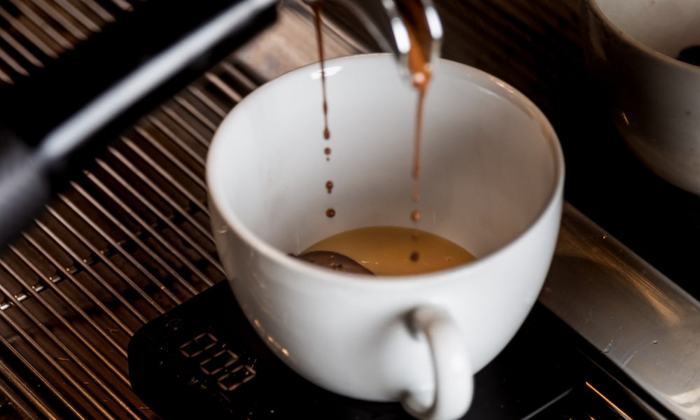 เอสเพรสโซ่กำลังรินจากเครื่องชงกาแฟลงในแก้วสีขาวที่วางอยู่บน ที่เที่ยวแก่งคอย ตาชั่งดิจิตอล เหมาะเป็นอย่างยิ่งสำหรับการเพลิดเพลินก่อนออกไปสำรวจที่เที่ยวแก่งคอย หรือวางแผนการเดินทางครั้งต่อไปที่เที่ยวชะอมแก่งคอย.