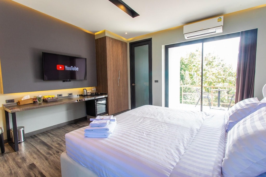 ห้องพักในโรงแรมทันสมัยพร้อมเตียงคู่ ทีวีติดผนังพร้อมโลโก้ YouTube บริเวณโต๊ะพร้อมสิ่งอำนวยความ เขาค้อที่พัก สะดวก และประตูกระจกสู่ระเบียงพร้อมที่นั่งกลางแจ้ง เหมาะสำหรับผู้ที่กำลังมองหาหาดเจ้าหลาวติดทะเลในความสะดวกสบายและมีสไตล์.