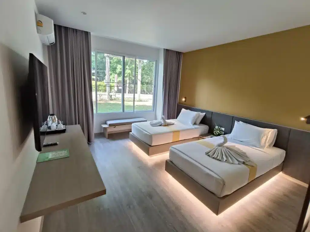 ห้องพักในโรงแรมทันสมัยพร้อมเตียงคู่ 2 เตียง ทีวีติดผนัง และหน้าต่างบานใหญ่ที่มองเห็นวิวเมือง เหมาะ เที่ยวแก่งคอย สำหรับแขกที่ออกสำรวจเที่ยวแก่งคอยหรือสำรวจที่เที่ยวชะอมแก่งคอย ผ้าเช็ดตัวถูกพับไว้อย่างเรียบร้อยในแต่ละเตียง การตกแต่งแบบเรียบง่ายทั่วทั้งห้อง.