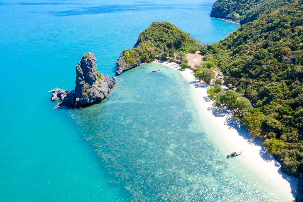 มุมมองทางอากาศของชายหาดอันเงียบสงบที่มีน้ำทะเลสีฟ้าครามใส  ที่เที่ยวเกาะสมุย ทรายขาว เนินเขาเขียวชอุ่ม และโขดหินที่ยื่นออกไปในทะเล เหมาะสำหรับผู้ที่แสวงหาเที่ยวสมุยในบรรยากาศอันเงียบสงบ.