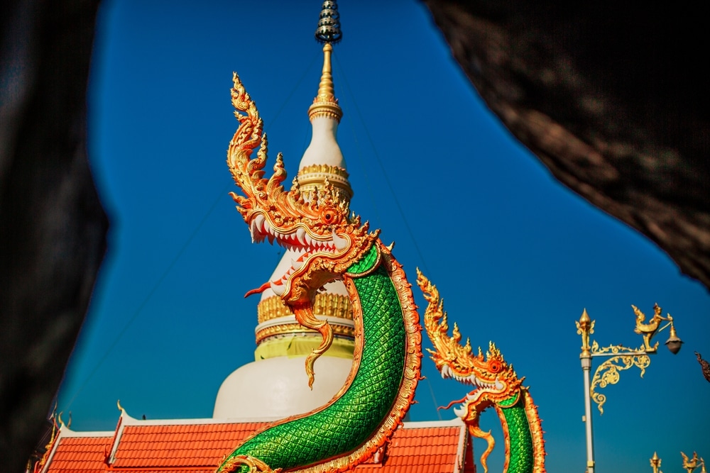 รูปปั้นมังกรสีทองที่มีชีวิตชีวาตั้งอยู่ ที่เที่ยวแก่งคอย ด้านหน้าเจดีย์สีขาวและสีทองภายใต้ท้องฟ้าสีฟ้าใส ซึ่งเป็นหนึ่งในไฮไลท์เมื่อคุณท่องเที่ยวแก่งคอยและสำรวจที่เที่ยวชะอมแก่งคอย.