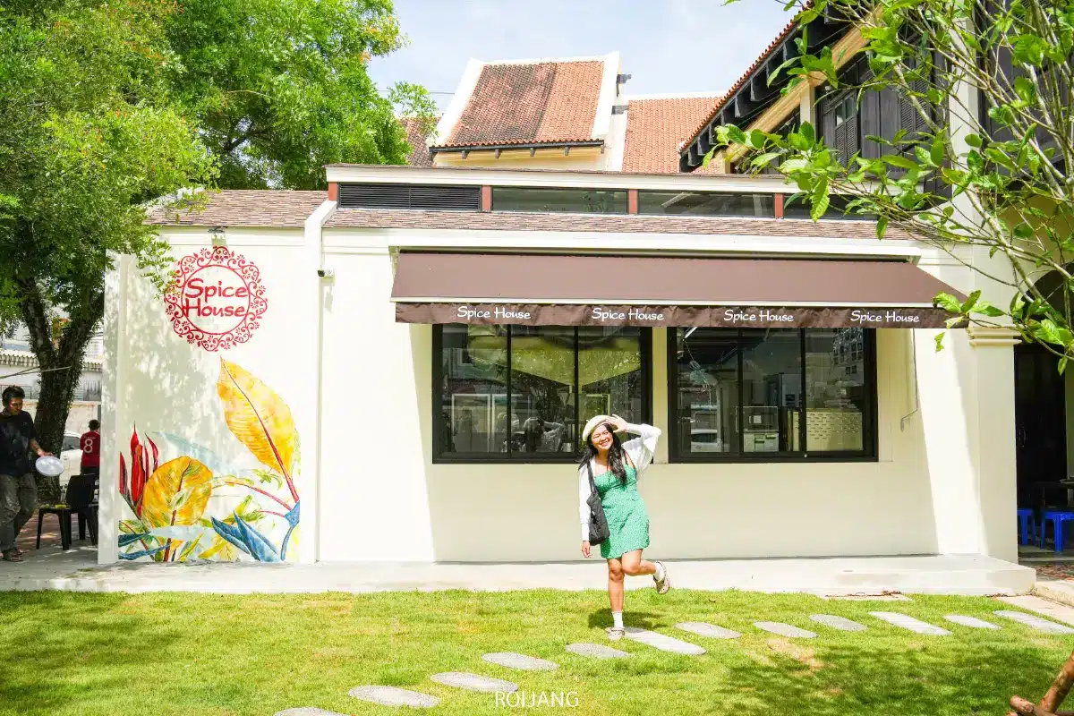 ผู้หญิงในชุดสีเขียวและหมวกสีขาวโพสท่าบนทางเดินหินด้านนอกร้าน Spice House ขณะเพลิดเพลินกับแสงแดด.