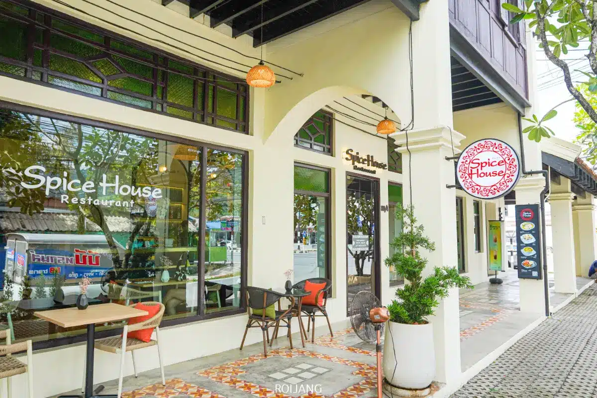 วิวภายนอกของร้าน Spice House ที่มีโต๊ะ เก้าอี้ และกระถางต้นไม้บนทางเท้าที่ปูกระเบื้องใต้ทางเดินที่มีหลังคา บรรยากาศที่น่าดึงดูดทำให้ร้าน Spice House เหมาะสำหรับการรับประทานอาหารกลางแจ้งในบรรยากาศที่มีชีวิตชีวา.