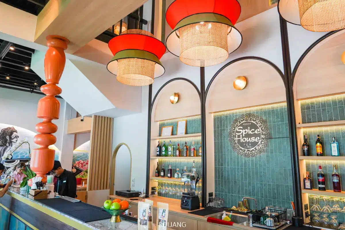 ร้านอาหาร Spice House มีการตกแต่งภายในที่ทันสมัย โดดเด่นด้วยโคมไฟสีแดงแขวน พื้นที่บาร์ที่มีชีวิตชีวาพร้อมขวดและผลไม้ และป้ายประจำร้านที่ปรากฏอยู่บนผนังกระเบื้องสีเขียวอันโดดเด่น.