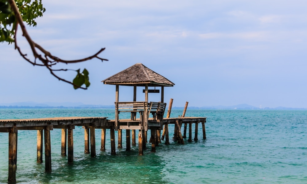 ท่าเรือไม้พร้อมที่พักขนาดเล็กทอดยาวเหนือน้ำทะเลสีฟ้าครามภายใต้ เที่ยวเกาะเสม็ด ท้องฟ้าที่มีเมฆบางส่วน มอบทิวทัศน์อันเงียบสงบ เหมาะสำหรับทุกคนที่กำลังมองหาเที่ยวเกาะเสม็ด และค้นพบหนึ่งในเกาะชั้นนำที่เที่ยวเกาะเสม็ด.