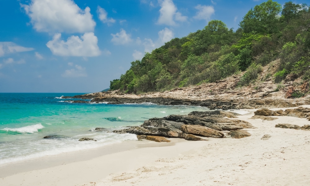 หาดทรายที่มีน้ำทะเลสีฟ้าครามใส แนวชายฝั่งหิน และต้นไม้สีเขียวใต้ท้องฟ้าสีคราม เหมาะสำหรับผู้ที่มองหา เที่ยวเสม็ด และเพลิดเพลินไปกับความงามตามธรรมชาติของเกาะ.