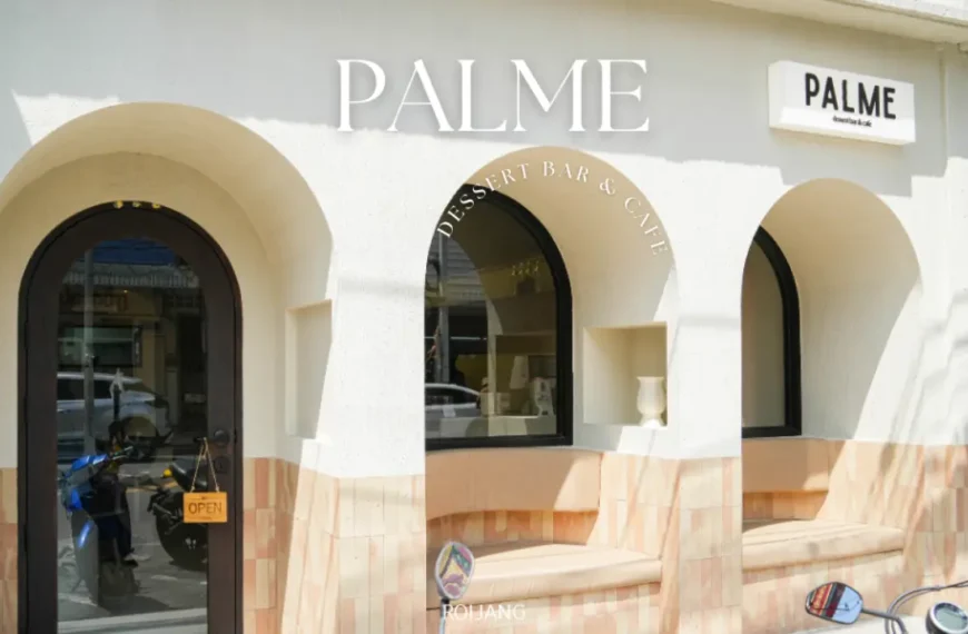 ภายนอกของ PALME Dessert Bar & Café มีหน้าต่างโค้ง ป้ายต้อนรับ "เปิด" ที่ประตู และผนังสีอ่อนพร้อมสีแทนที่ช่วยเน้นให้บรรยากาศอันน่าดึงดูดของ PALME.