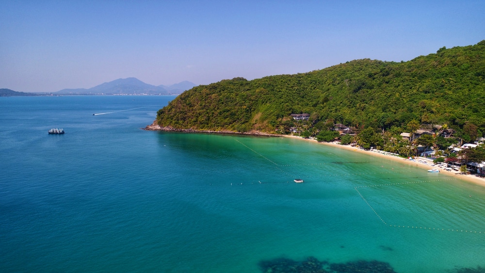 วิวทางอากาศของแนวชายฝั่งเขตร้อนที่เที่ยวเกาะเสม็ด พร้อมน้ำทะเลสีฟ้าครามใส หาดทราย และเนินเขาเขียวขจีภายใต้ท้องฟ้าสีครามสดใส เหมาะสำหรับผู้ที่มองหาเที่ยวเกาะเสม็ดและผ่อนคลายในสวรรค์.