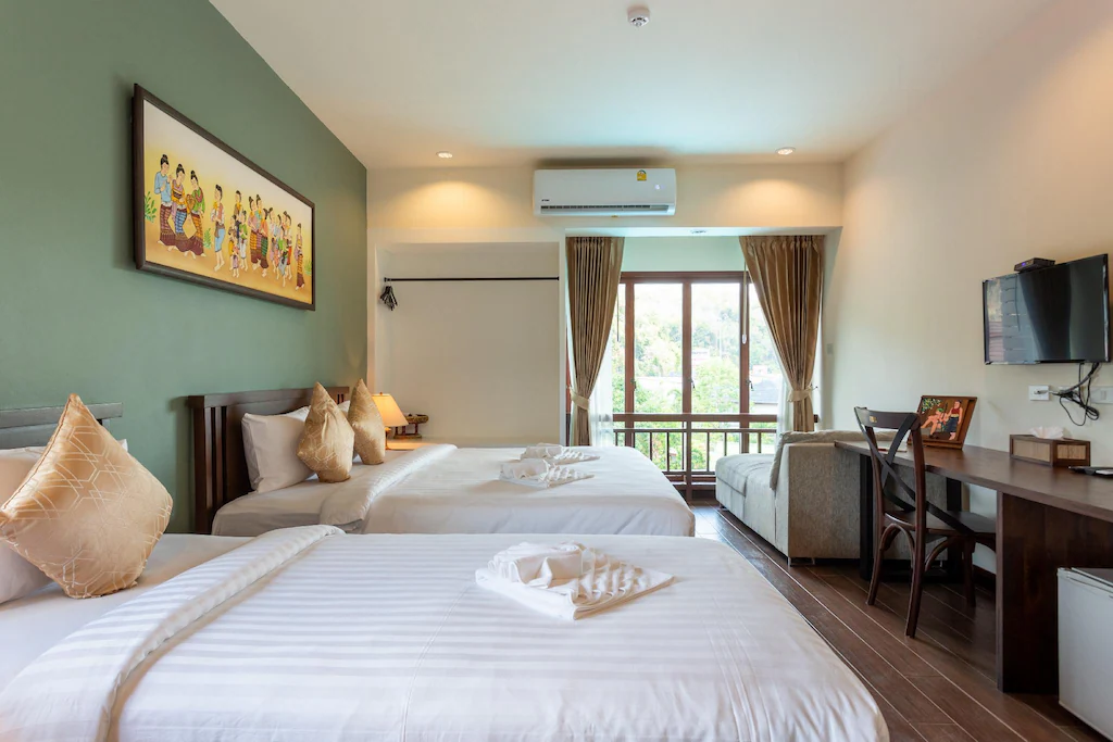 ห้องพักในโรงแรมที่มีเตียงคู่ 2 เตียง ทีวีติดผนัง โต๊ะพร้อมเก้าอี้ โซฟา  ที่พักสตูลแนวธรรมชาติ หน้าต่างบานใหญ่พร้อมผ้าม่าน และภาพวาดเหนือเตียง เหมาะสำหรับผู้ที่กำลังมองหาที่พักสไตล์ธรรมชาติและความสะดวกสบายที่ทันสมัย.