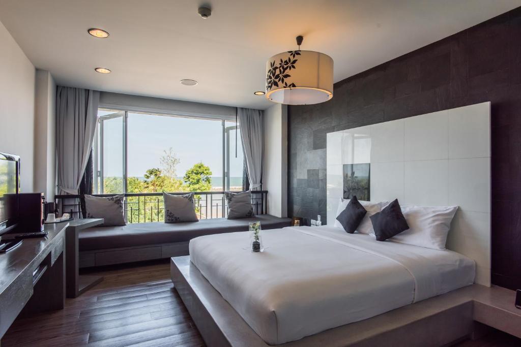 ห้องพักโรงแรมสมัยใหม่พร้อมเตียงขนาดใหญ่ การตกแต่งสีดำและขาว ที่นั่งริมหน้าต่าง โทรทัศน์จอแบน และวิวต้นไม้และท้องฟ้า—ตัวเลือกที่เหมาะสำหรับใครก็ตามที่กำลังมองหาที่พักชะอำในสไตล์และความสะดวกสบาย.