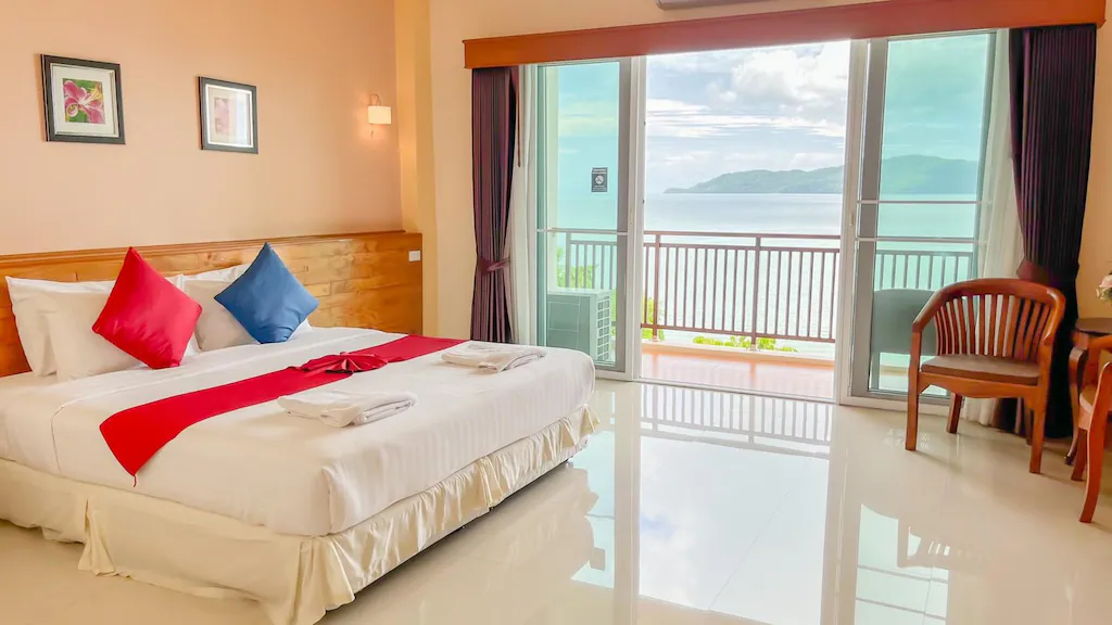 ห้องพักในโรงแรมพร้อมเตียงคู่ เฟอร์นิเจอร์ไม้ และประตูกระจกบาน ที่พักสตูลแนวธรรมชาติ ใหญ่ที่เปิดออกสู่ระเบียงพร้อมวิวทะเลและภูเขา เหมาะสำหรับผู้ที่กำลังมองหาที่พักสไตล์ธรรมชาติ.