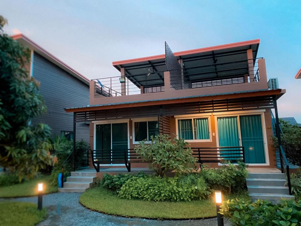 บ้านสไตล์โมเดิร์น 2 ชั้นที่มีดาดฟ้า หน้าต่างบานใหญ่ และรายล้อมไปด้วยต้นไม้ ถ่ายภาพในเวลาพลบค่ำโดยเปิดไฟภายนอกไว้.