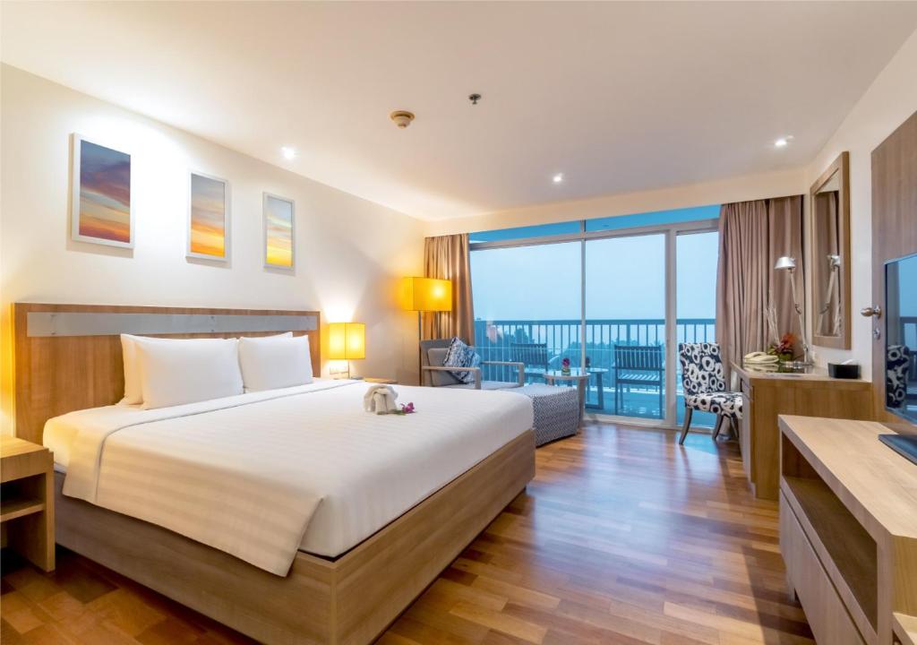 ห้องพักโรงแรมสมัยใหม่พร้อมเตียงขนาดใหญ่ พื้นไม้ พื้นที่นั่งเล่น โต๊ะทำงาน โทรทัศน์ และระเบียงที่สามารถมองเห็นวิวผ่านประตูกระจก—เหมาะสำหรับผู้ที่ต้องการที่พักชะอำ หรือที่พักในชะอำที่ทั้งมีสไตล์และสะดวกสบาย.