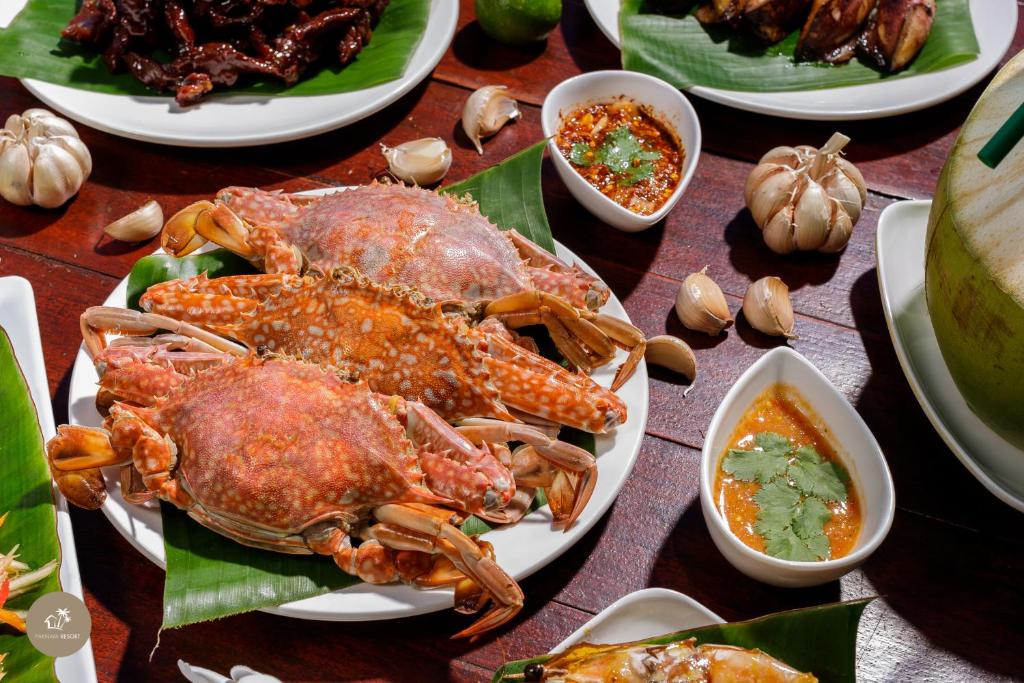 ปูปรุงสุกสองตัวเสิร์ฟบนจานสีขาวพร้อมใบตอง ล้อมรอบด้วยน้ำจิ้มและ ที่พักสตูลแนวธรรมชาติ กลีบกระเทียม ให้รสชาติที่แท้จริงของทะเล เหมาะสำหรับนักเดินทางที่กำลังมองหาสตูลแนวธรรมชาติและรสชาติท้องถิ่น.