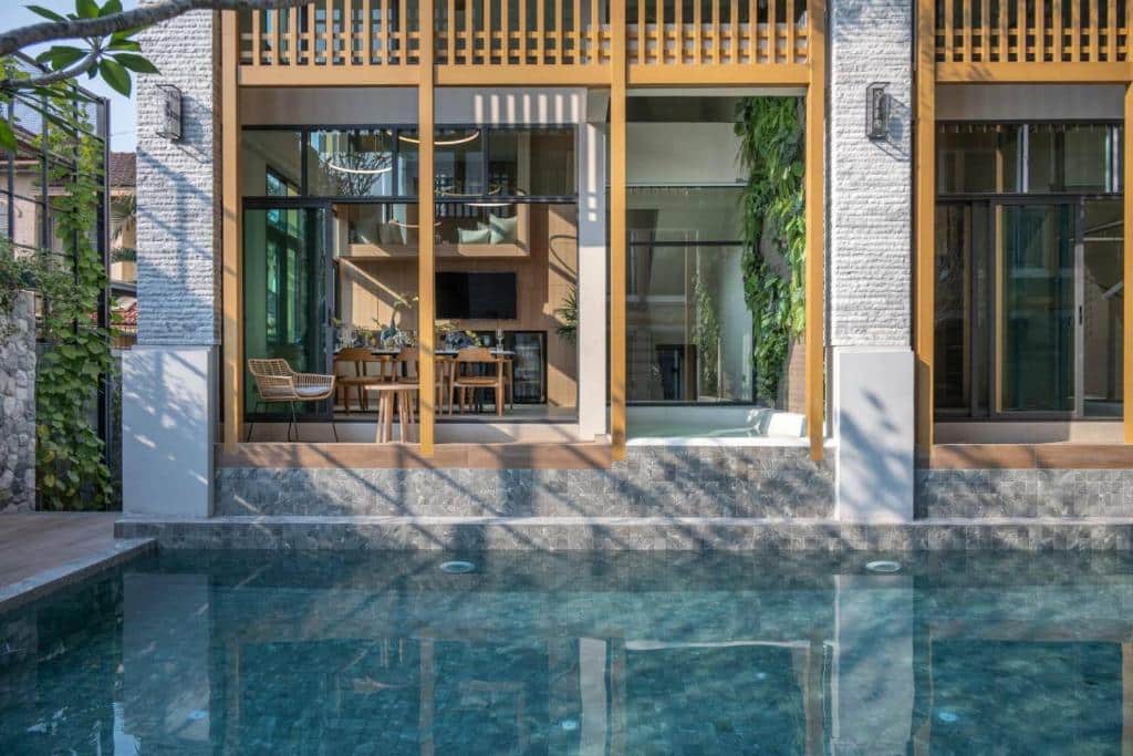 บ้านสไตล์โมเดิร์นที่มีหน้าต่างกระจกบานใหญ่มองเห็นสระว่ายน้ำที่ใสสะอาด ภายในมีพื้นที่รับประทานอาหารและพื้นที่สีเขียว.