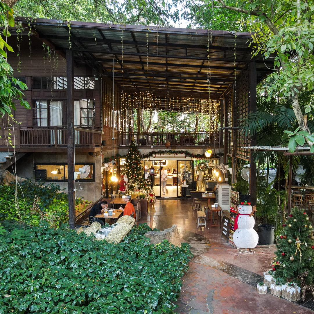 คาเฟ่บรรยากาศสบายๆ พร้อมที่นั่งทั้งกลางแจ้งและในร่ม ตกแต่งในวันหยุด เช่น ต้นคริสต์มาสและตุ๊กตาหิมะ ล้อมรอบด้วยแมกไม้เขียวขจีใต้แสงไฟประดับ เหมาะสำหรับการพักผ่อนขณะสำรวจพื้นที่ตาก.