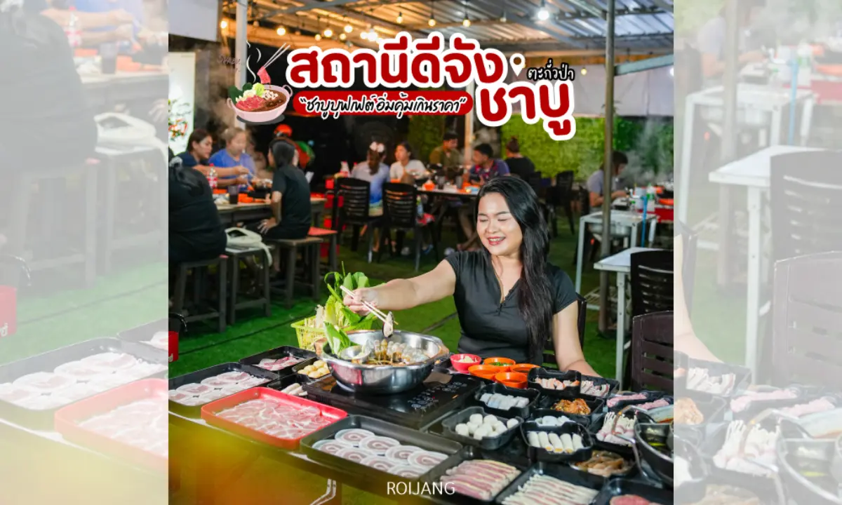 ผู้หญิงคนหนึ่งนั่งอยู่ที่โต๊ะกลางแจ้ง กำลังปรุงเนื้อสัตว์และผักต่าง ๆ บนเตาปิ้งย่างร้อน ๆ ที่ สถานีดีจัง ล้อมรอบด้วยจานอาหารหลายอย่าง และมีผู้รับประทานอาหารคนอื่น ๆ อยู่เบื้องหลัง.