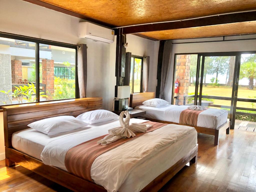 ห้องพักในโรงแรมที่มี 2 เตียง ผ้าปูที่นอนสีขาว รันเนอร์สีน้ำตาล ผ้าเช็ดตัวหงส์บนเตียง พื้นไม้  ที่พักสตูลแนวธรรมชาติ หน้าต่างบานใหญ่ ทัศนียภาพของต้นไม้และต้นไม้เขียวขจีด้านนอก เหมาะอย่างยิ่งสำหรับคนรักธรรมชาติ.