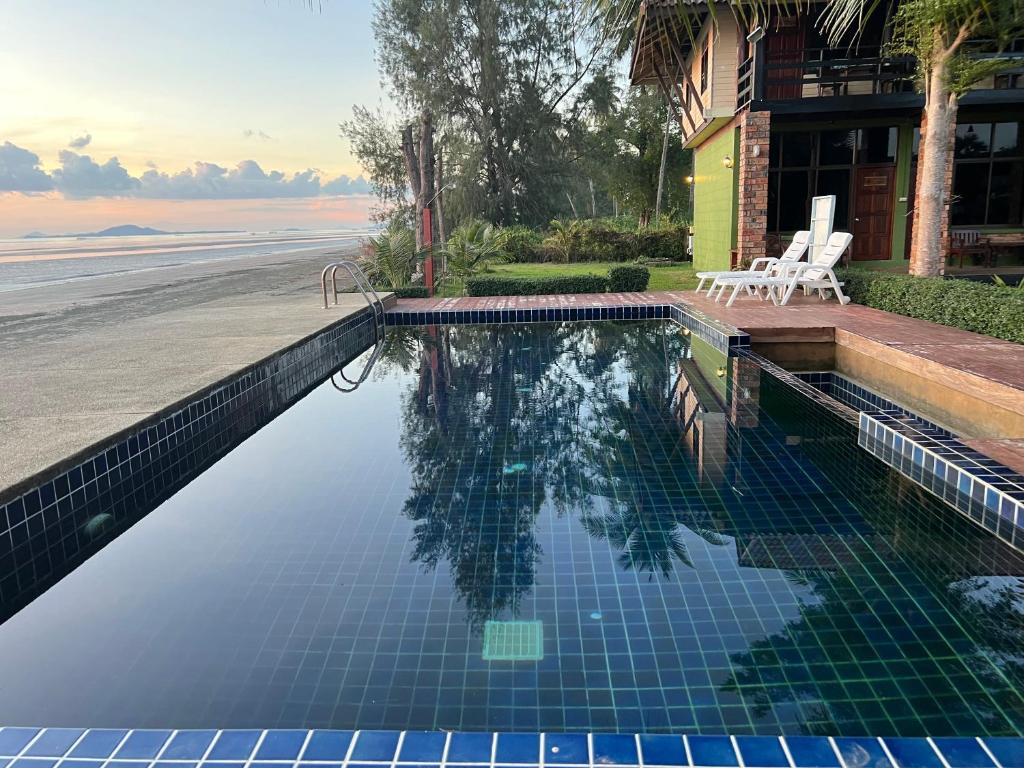 สระว่ายน้ำรูปสี่เหลี่ยมผืนผ้าข้างลานบ้านพร้อมเก้าอี้นั่งเล่น ติดกับหาดทรายและมหาสมุทร ล้อมรอบด้วย ที่พักสตูลแนวธรรมชาติ ต้นไม้และอาคารในเวลาพระอาทิตย์ขึ้นหรือพระอาทิตย์ตก เหมาะสำหรับผู้ที่กำลังมองหาที่พักสตูลแนวธรรมชาติ.