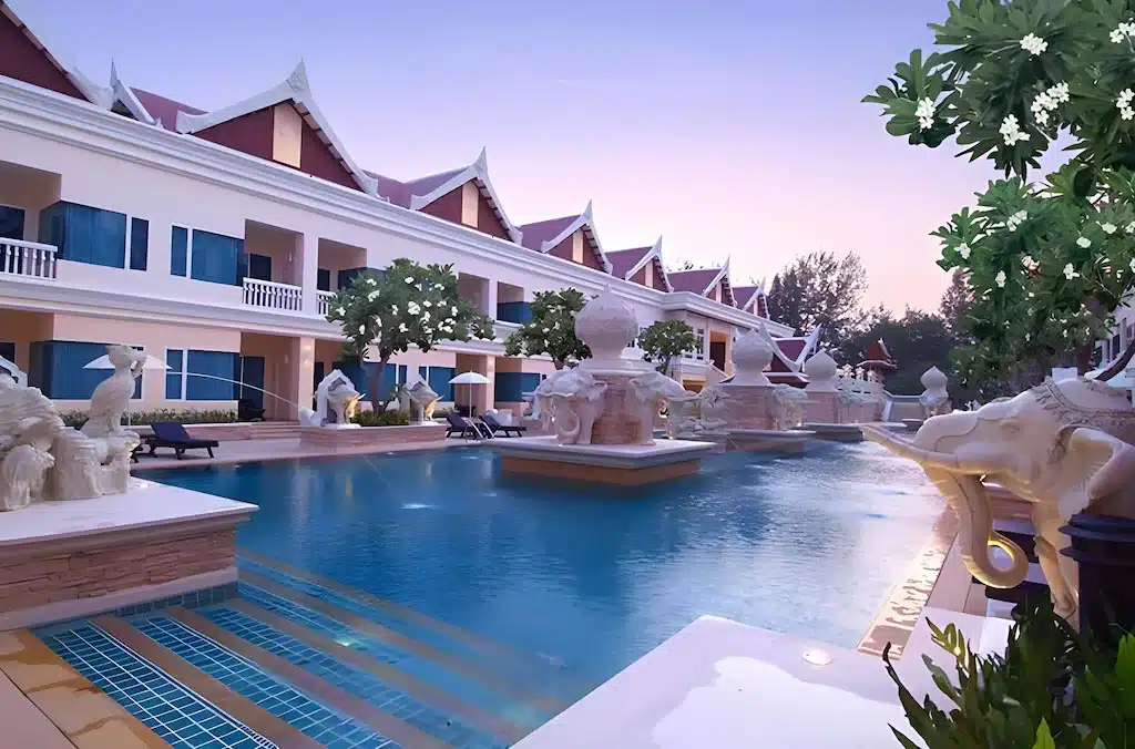 โรงแรมหรูพร้อมสระว่ายน้ำกลางแจ้ง ประติมากรรมที่ประดับประดาอย่างวิจิตร และอาคารสองชั้นสีขาวที่มีหลังคาสีแดงโดดเด่นยามพระอาทิตย์ตก—เหมาะอย่างยิ่งสำหรับผู้ที่มองหา โรงแรมชะอำ ในบรรยากาศที่สวยงามตระการตา.