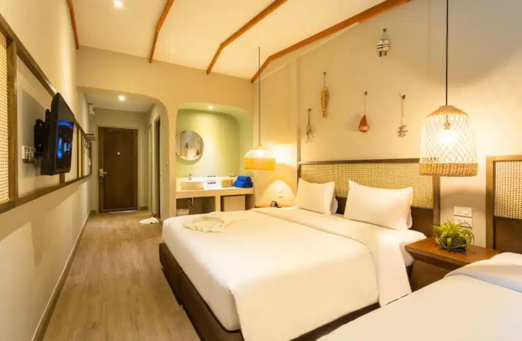 ห้องพักในโรงแรมที่มีเตียงคู่ 2 เตียง หัวเตียงหวาย โคมไฟแขวน อุปกรณ์ตกแต่งผนัง ทีวีจอแบน และพื้นที่โต๊ะเครื่องแป้งแบบเปิดใกล้ทางเข้า  ที่พักสตูลแนวธรรมชาติ เหมาะสำหรับผู้ที่กำลังมองหาสตูลแนวธรรมชาติที่มีความสะดวกสบายและมีสไตล์.