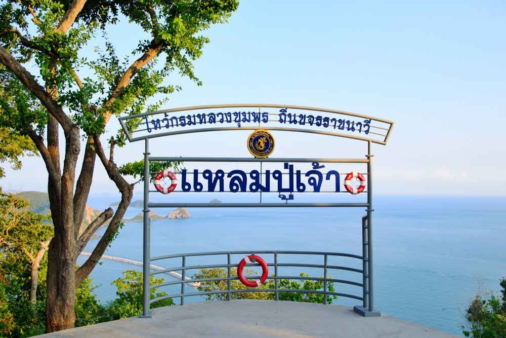 จุดชมวิวที่มีป้ายภาษาไทยมองเห็นทะเลและเกาะต่างๆ ล้อมรอบด้วยต้นไม้และท้องฟ้าสดใส เหมาะสำหรับผู้ที่ค้นหาที่เที่ยวสัตหีบหรือสถานที่เงียบสงบในการเที่ยวสัตหีบ.