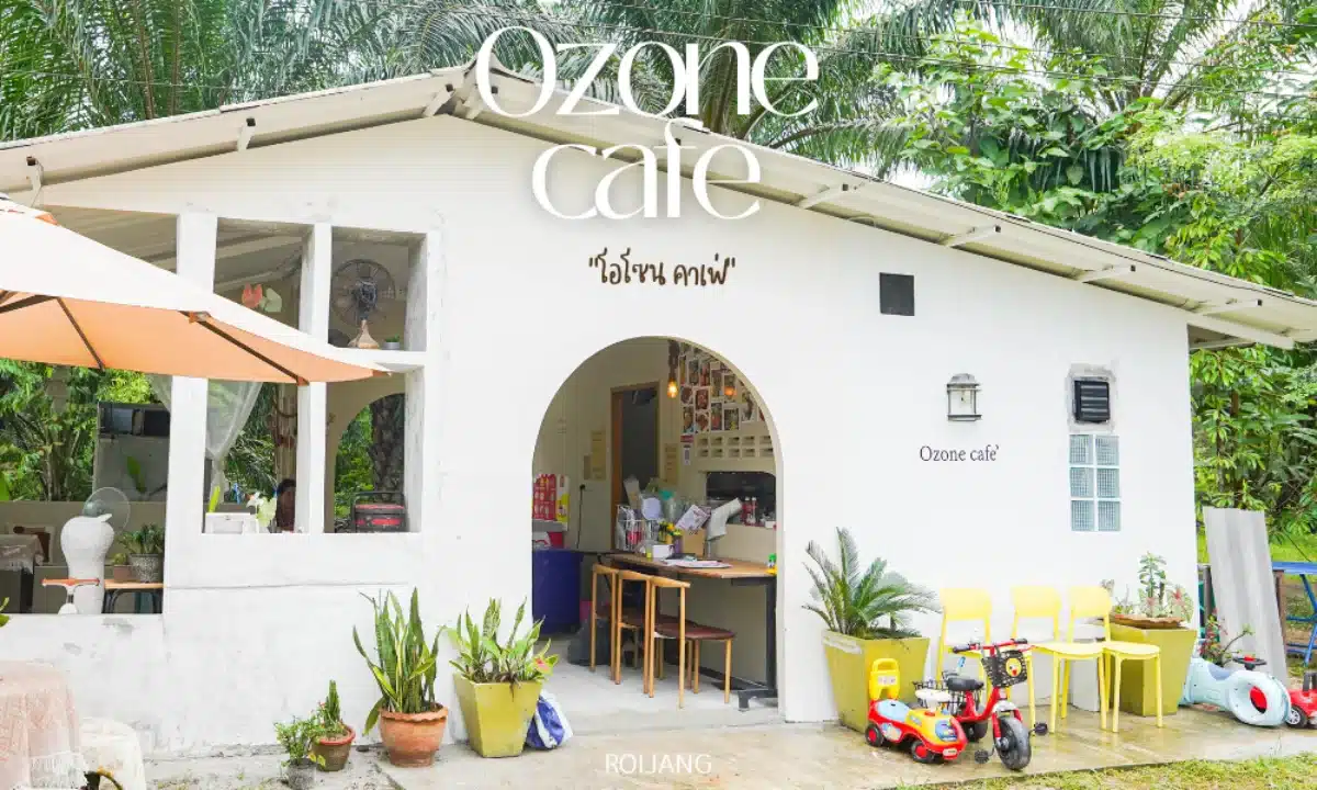 อาคารสีขาวขนาดเล็กที่มีป้ายเขียนว่า "โอโซนคาเฟ่" พร้อมเก้าอี้สีเหลือง ต้นไม้ในกระถาง และของเล่นเด็กอยู่ด้านนอก ล้อมรอบด้วยพืชพรรณสีเขียว เป็น สถานีดีจัง ที่น่าเชิญชวนสำหรับครอบครัว.