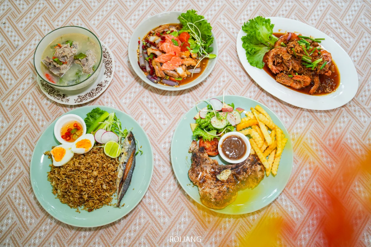 จานอาหารไทยห้าจานถูกจัดวางบนผ้าปูโต๊ะลายที่ Ozone Cafe ประกอบด้วยเนื้อย่างกับเฟรนช์ฟราย ข้าวผัดกับไข่ ซุป สลัด และกุ้งราดซอส.