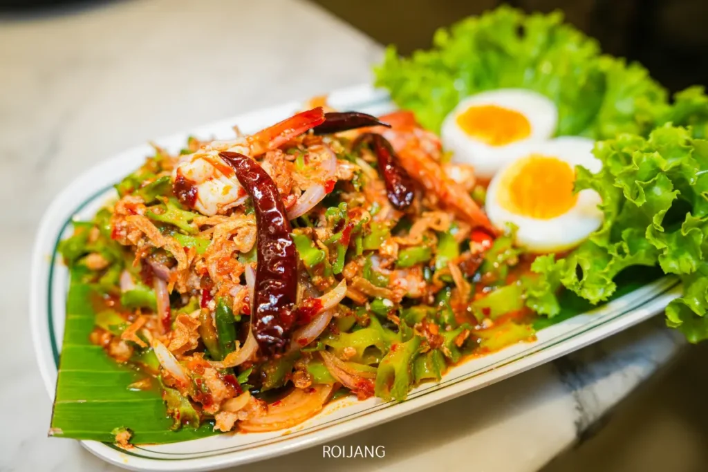 จานสลัดลาวญวนรสเผ็ดกับกุ้ง พริกแห้ง ผัก และหัวหอมแดง เสิร์ฟพร้อมผักกาดหอมและไข่ลวกครึ่งฟองสองฟอง.