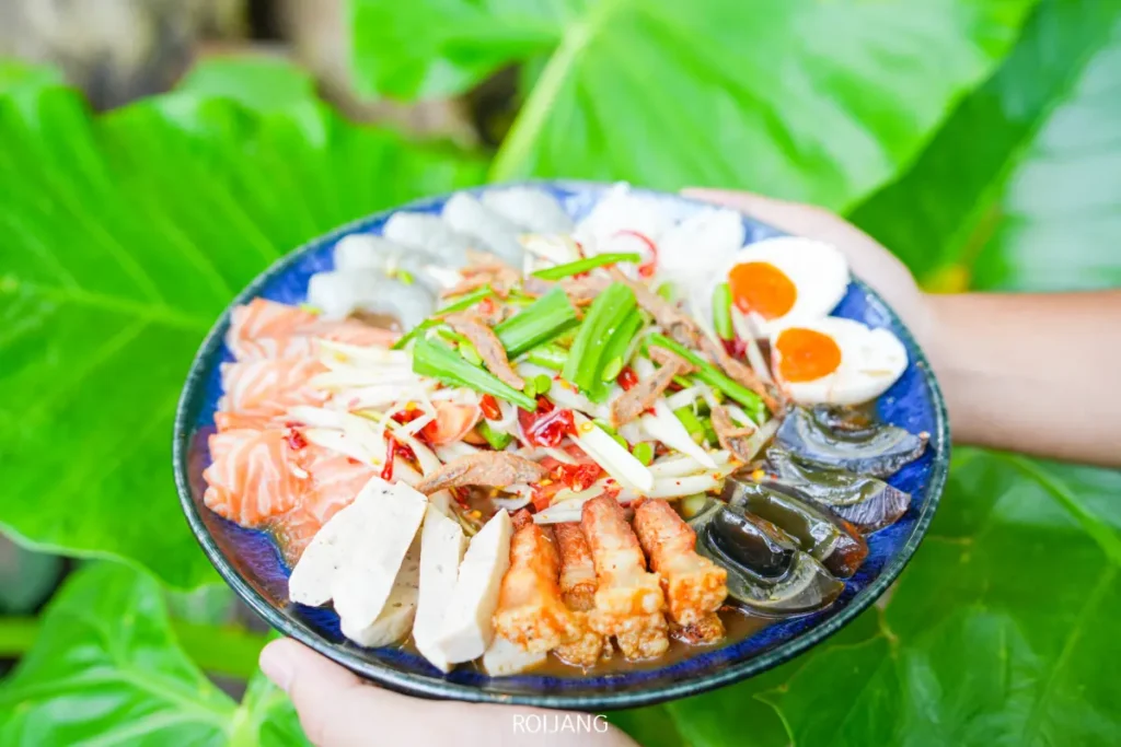 จานรวมอาหารทะเลและเนื้อสัตว์สไตล์ไทยหลากหลายชนิด ประกอบด้วยแซลมอน กุ้ง ไข่เยี่ยวม้า ไส้กรอกหั่นแว่น และไข่ลวก ตกแต่งด้วยสมุนไพรสดและพริกในสไตล์แอบแอฟิวชั่นแท้ๆ.