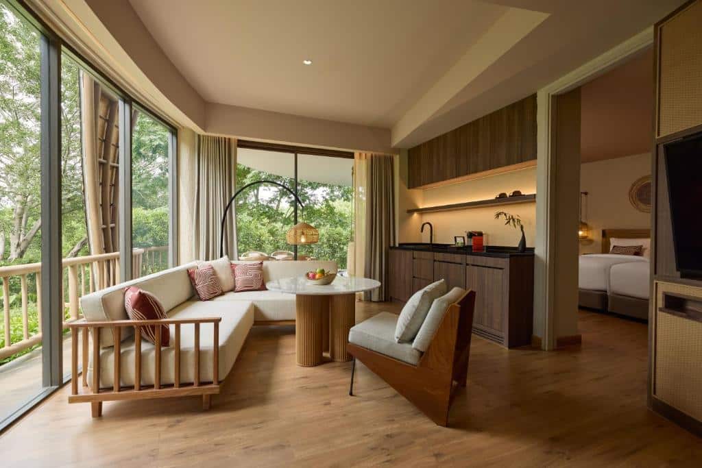 ห้องสวีทโรงแรมสมัยใหม่พร้อมหน้าต่างบานใหญ่ พื้นที่นั่งเล่นที่อบอุ่น มุมครัว และห้องนอนที่มองเห็นได้ผ่านประตูเปิด เพลิดเพลินกับพืชพรรณเขียวขจีภายนอก เหมาะสำหรับการเข้าพักของคุณที่ โรงแรมเขาใหญ่ ด้วยความสะดวกสบายและสไตล์.