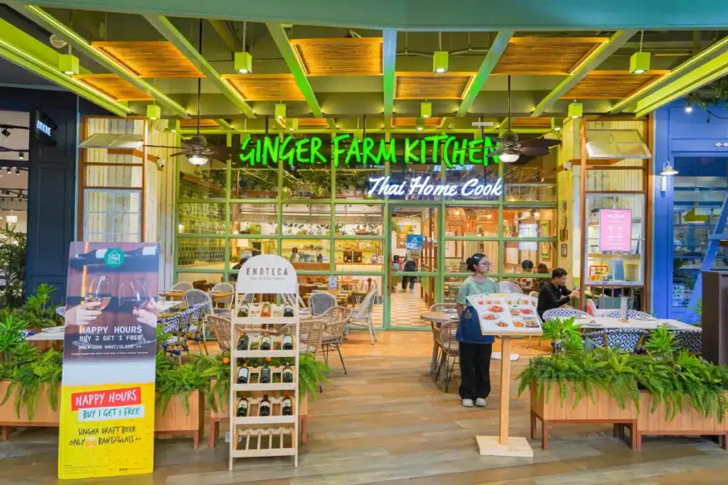 ร้านอาหารสว่างไสวชื่อว่า "Ginger Farm Kitchen" พร้อมป้ายไฟนีออนสีเขียว, แท่นโชว์เมนู, ต้นไม้, และผู้คนกำลังรับประทานอาหารทั้งภายในและภายนอก—เหมาะสำหรับผู้ที่กำลังค้นหา ร้านอาหารเซ็นทรัลภูเก็ต.