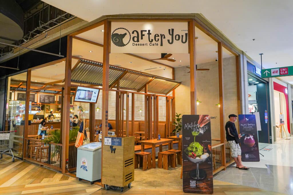 คาเฟ่ขนมหวานที่มีกรอบไม้ชื่อว่า "After You" ตั้งอยู่ในเซ็นทรัลภูเก็ตร้านอาหาร, มีที่นั่งในร่มที่แสนสบายและโปสเตอร์เครื่องดื่มขนาดใหญ่ที่ทางเข้า มีคนยืนอยู่ใกล้ๆ เชิญชวนให้คุณมาค้นพบความอร่อยของร้านอาหารในเซ็นทรัลภูเก็ต.