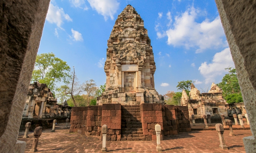 วัดหินโบราณที่มีลวดลายแกะสลักอย่างประณีตตั้งอยู่ใจกลางลานกว้าง ท่ามกลางท้องฟ้าสีครามและเมฆที่ ที่เที่ยวสระแก้ว กระจายตัวอยู่ เป็นสถานที่ท่องเที่ยวที่ต้องไปเยือนสำหรับผู้รักประวัติศาสตร์.