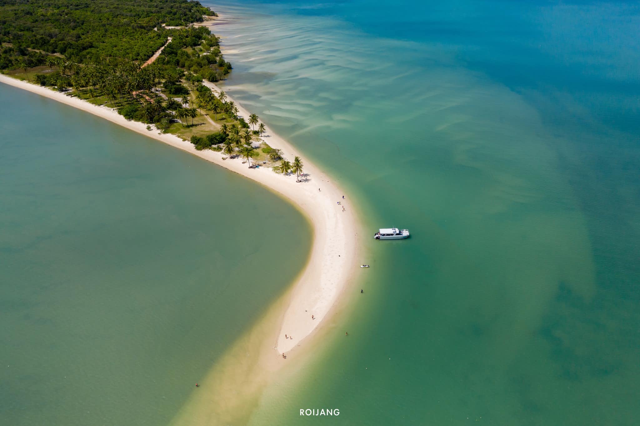 ภาพมุมสูงของชายหาดแคบที่ทอดยาวเชื่อมระหว่างสองผืนแผ่นดิน มีเรือจอดทอดสมออยู่กลางทะเล และทิวทัศน์ของธรรมชาติเขียวขจีเบื้องหลัง—หนึ่งในสถานที่ท่องเที่ยวสุดตระการตาของ เที่ยวตะกั่วป่า ที่คุณไม่ควรพลาด.