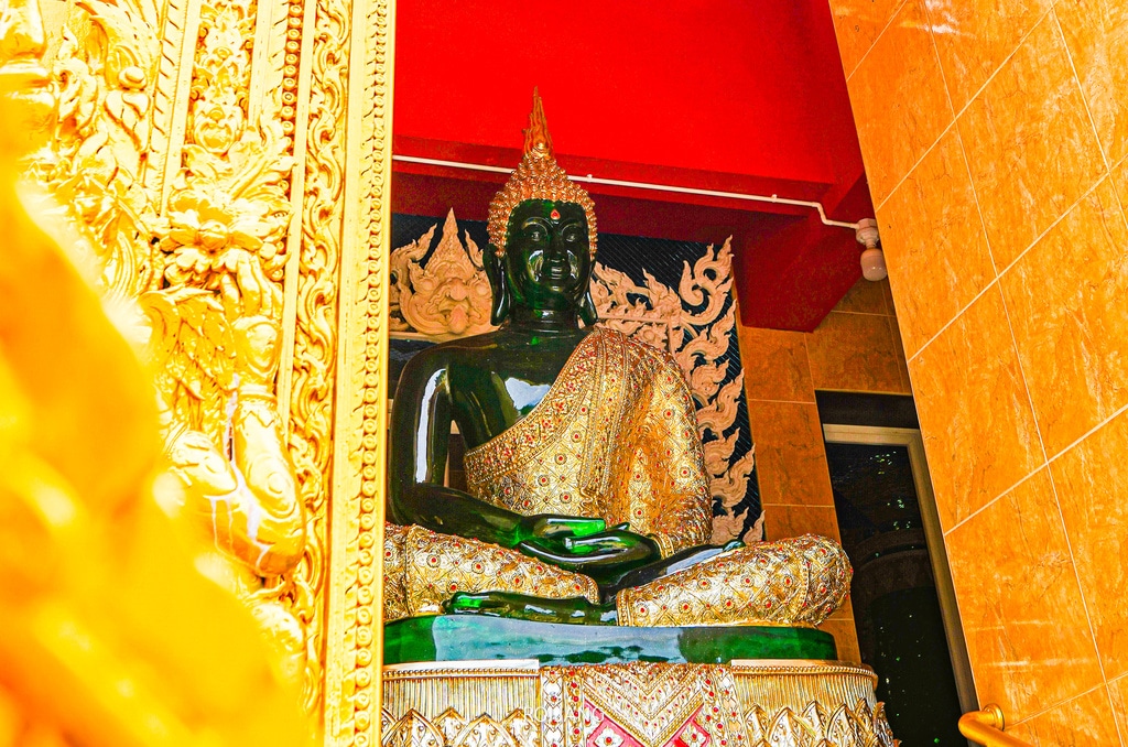 พระพุทธรูปสีดำในพระอุโบสถทองคำที่ประดับประดาอย่างงดงาม พร้อมเพดานสีแดงและลวดลายประดับประดาอย่างละเอียดในฉากหลัง—ภาพที่เป็นสัญลักษณ์ของสถานที่ท่องเที่ยวที่นักท่องเที่ยวที่รักวัฒนธรรมไม่ควรพลาดใน เที่ยวตะกั่วป่า