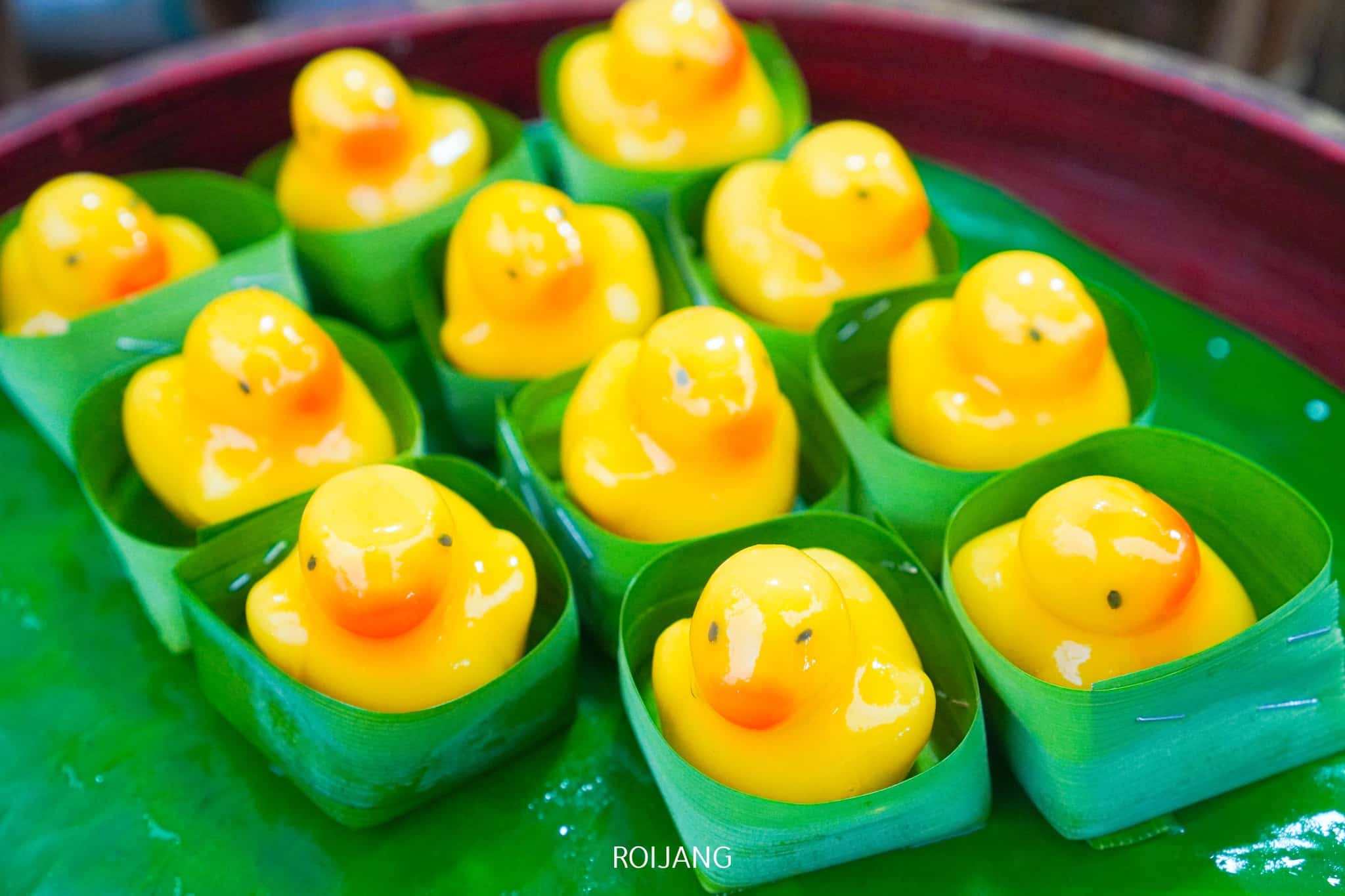 ขนมหวานรูปเป็ดสีเหลืองถูกจัดวางในใบไม้สีเขียวบนถาดสีเขียว เพิ่มความสนุกสนานให้กับอาหารอันน่ารื่นรมย์ที่คุณสามารถพบได้ที่ ที่เที่ยวตะกั่วป่า.