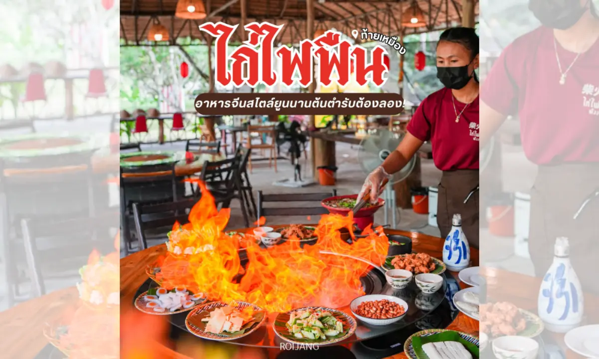 พนักงานร้านอาหารสวมหน้ากากกำลังเสิร์ฟอาหารบนโต๊ะที่มีเปลวไฟลุกโชนจากจานไก่ไฟฟืน มีอาหารไทยหลากหลายชนิดจัดแสดงอยู่ และลูกค้าต่างนั่งรับประทานอาหารอยู่ด้านหลัง.