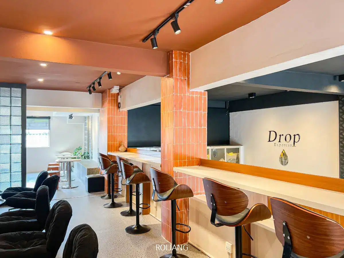 ร้านกาแฟสมัยใหม่ตกแต่งภายในด้วยเก้าอี้บาร์ไม้ที่เคาน์เตอร์ เก้าอี้เลานจ์สีดำ และป้ายที่เขียนว่า "Drop Espresso" บนผนัง Pause Coffee Bar มอบพื้นที่สว่าง สะอาด และสว่างไสวให้คุณได้ผ่อนคลายและเพลิดเพลินกับกาแฟที่คุณชื่นชอบ.