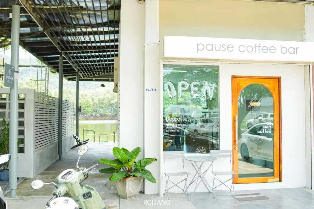 Pause Coffee Bar ยินดีต้อนรับคุณด้วยป้ายเปิดร้านที่เปิดต้อนรับ ที่นั่งกลางแจ้งที่เชิญชวน และบรรยากาศที่อบอุ่น—สังเกตสกู๊ตเตอร์ที่จอดอยู่ใกล้ๆ ขณะที่คุณจิบกาแฟแก้วโปรดของคุณ.