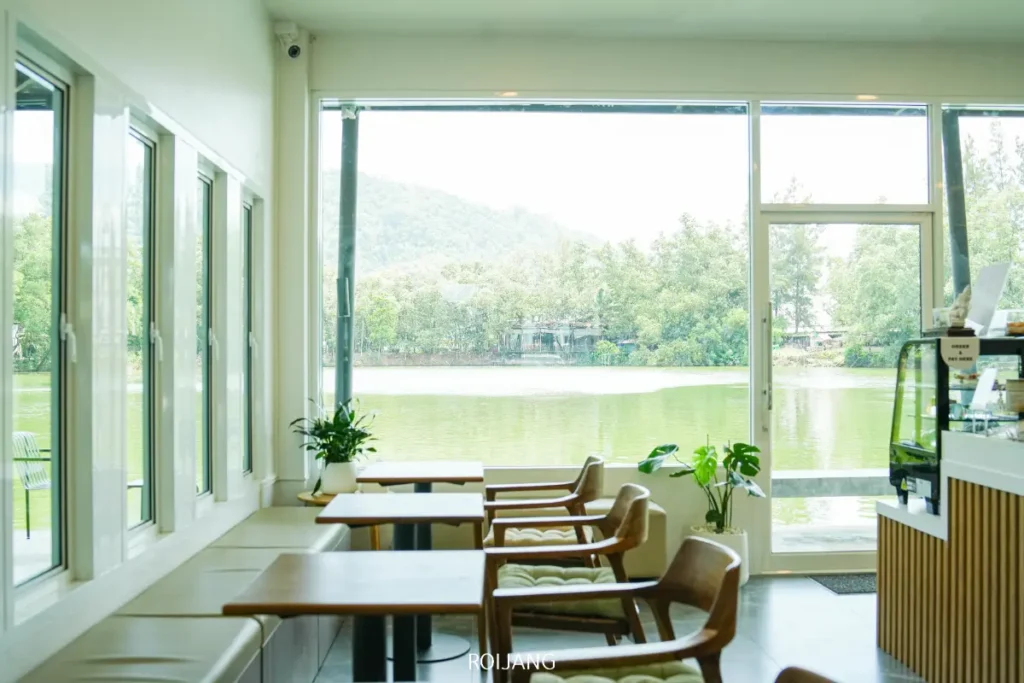 Pause Coffee Bar เป็นคาเฟ่สมัยใหม่ที่มีโต๊ะและเก้าอี้ไม้ มองเห็นวิวจากหน้าต่างบานใหญ่ที่มองเห็นทะเลสาบและต้นไม้ภายนอกในช่วงเวลากลางวัน.