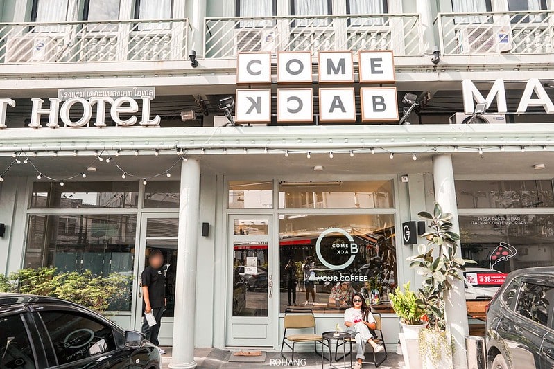 ผู้หญิงคนหนึ่งนั่งอยู่ด้านนอก "COME BACK" คาเฟ่ภูเก็ต สไตล์ภูเก็ตที่ตั้งอยู่บนชั้นล่างของอาคารซึ่งมีโรงแรมอยู่ด้านบน.